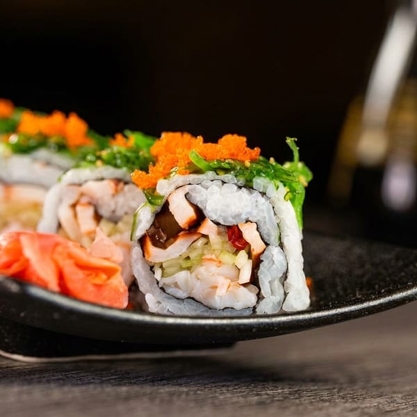 Sushi rolls with orange tobiko, green seaweed, and pickled ginger on a black plate.
