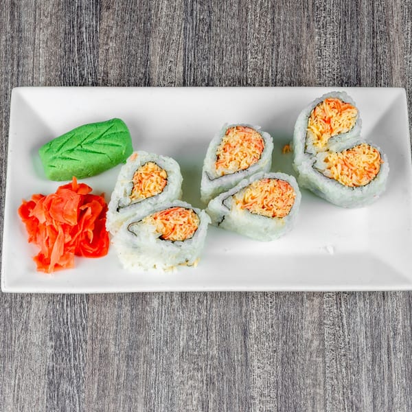 Six sushi rolls with crab meat, a green leaf-shaped wasabi, and pickled ginger on a white plate.