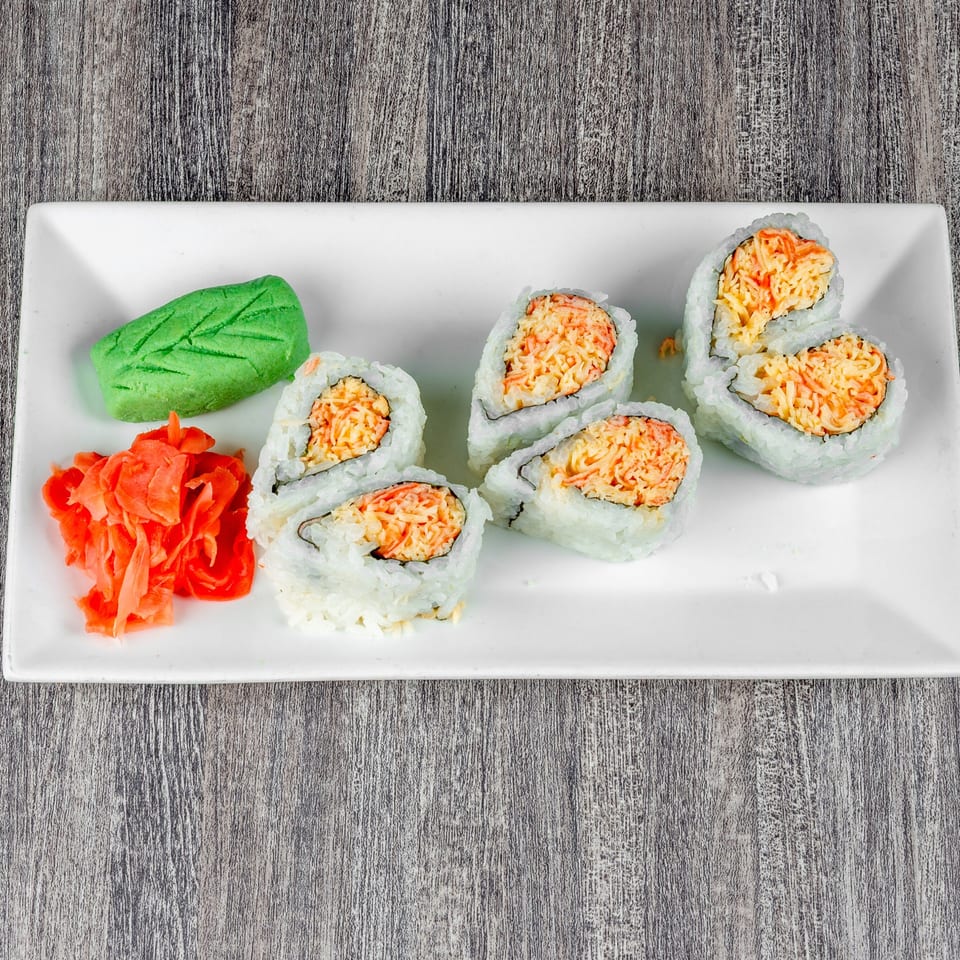 Six sushi rolls with crab meat, a green leaf-shaped wasabi, and pickled ginger on a white plate.
