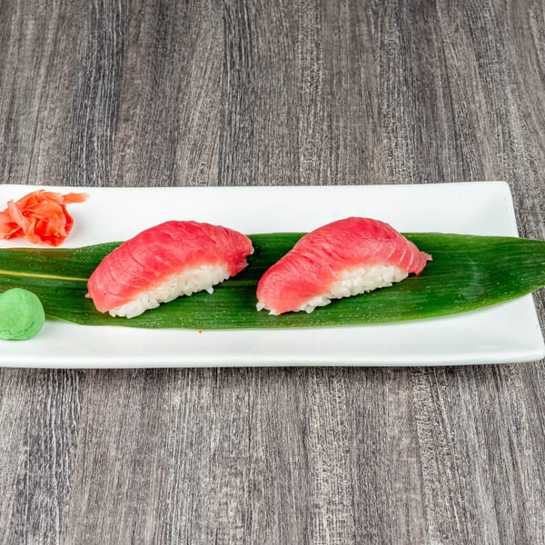 Two pieces of tuna nigiri sushi with wasabi and pickled ginger on a white plate.