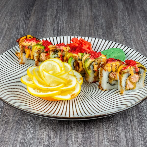 A plate of sushi rolls topped with red roe, sauce, and avocado, garnished with lemon slices.