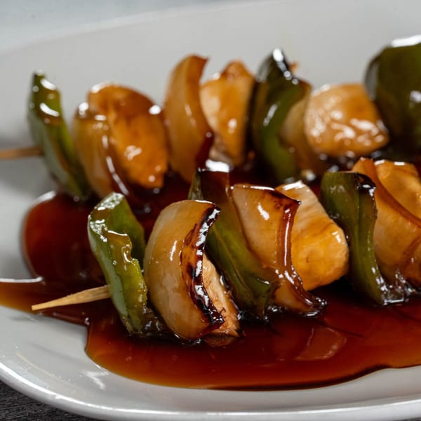 Sweet and sour chicken and green pepper skewers on a white plate with sauce.