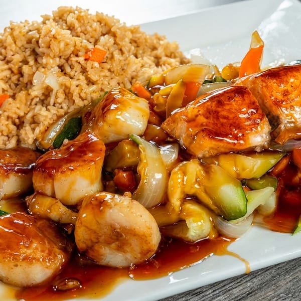 Hibachi scallops, salmon, and vegetables with fried rice on a white rectangular plate.