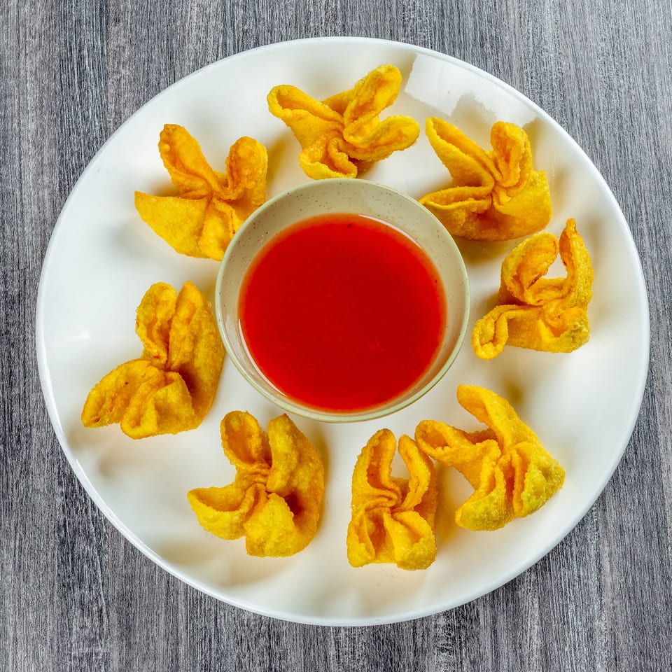 Crispy golden wontons arranged around a small bowl of vibrant red dipping sauce on a white plate.