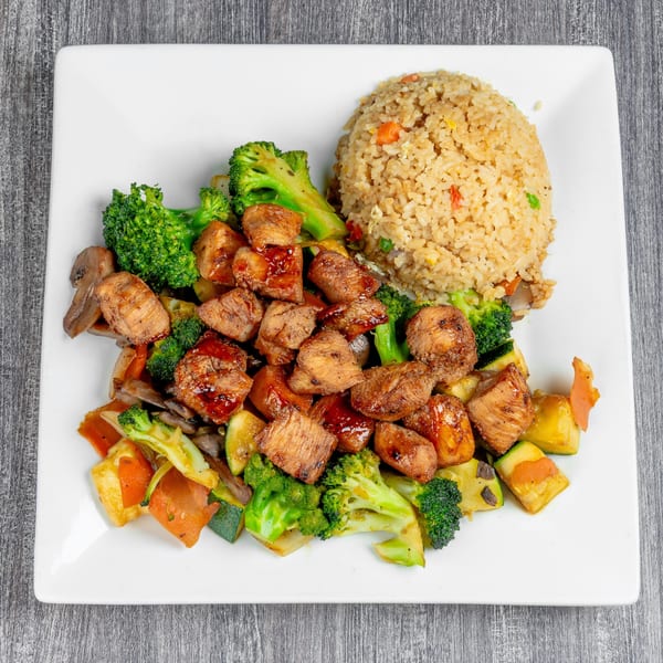 Teriyaki chicken with broccoli, zucchini, carrots, mushrooms, and a side of fried rice on a white plate.
