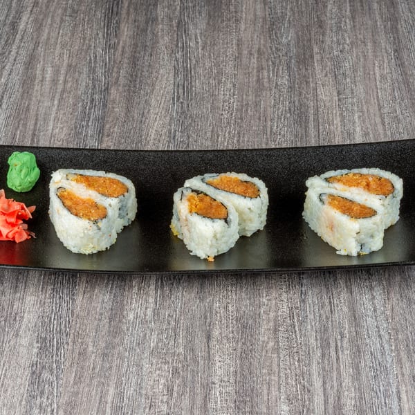 Three spicy tuna sushi rolls with wasabi and pickled ginger on a black rectangular plate.