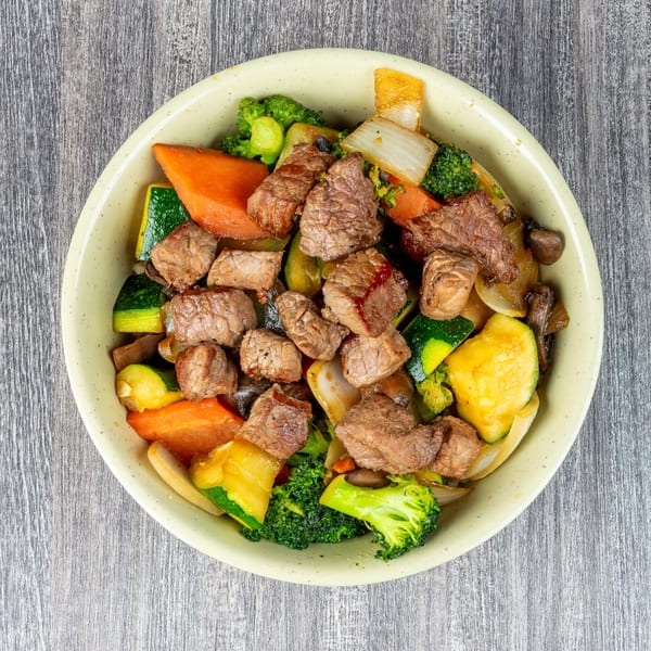 A bowl of steak and mixed vegetables, including broccoli, zucchini, carrots, and onions.