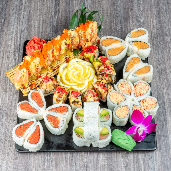 A large platter of various sushi rolls, including spicy tuna, California, and dragon rolls, garnished with lemon slices and an orchid.