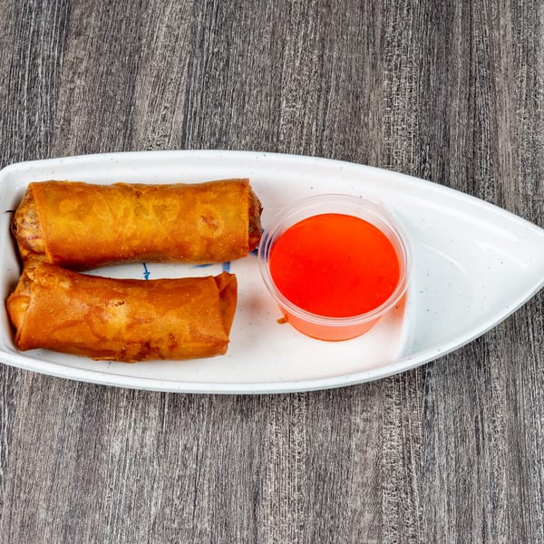 Two crispy golden egg rolls and a small cup of bright red sweet and sour sauce on a white plate.